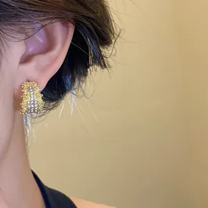 Close-up of elegant C-shaped gold stud earring with rhinestones on ear