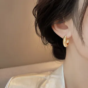 Close-up detail of stylish gold textured hoop earrings worn by a model for fashion look