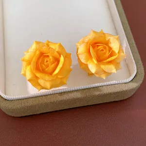 Close-up view of elegant yellow rose flower stud earrings inside a luxury jewelry display box.