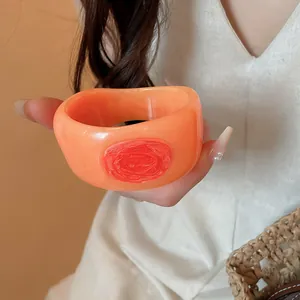 Detailed view of a chunky orange resin bangle featuring an artistic red marble swirl motif