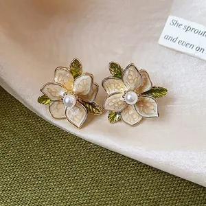 French style enamel flower stud earrings with pearls on textured fabric background.