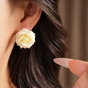 Close-up of a white rose flower stud earring worn by a model, 18K gold plated detail.