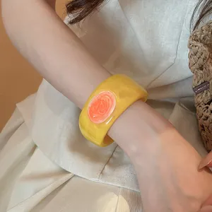 Close-up of a chunky yellow resin bangle with orange marbled drip oil design on a wrist