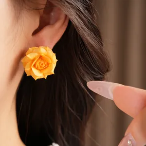 Detailed view of a yellow rose stud earring being worn on an ear for size context.