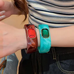 Detail view of chunky resin bangles with red and green square gemstones on wrist.