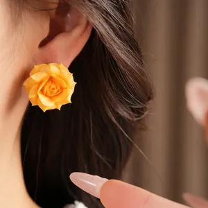 Detailed view of an elegant yellow rose flower stud earring worn on an Asian model's ear.