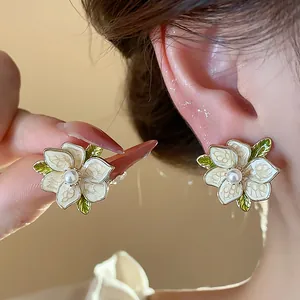 Close-up of French style white enamel flower earrings with pearl centers and green leaves