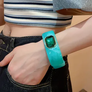 Close-up of a wide teal resin bangle with a large emerald green faceted gemstone.