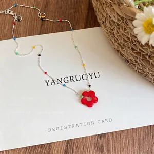 Detail of a colorful beaded necklace with a red flower pendant on a white registration card.