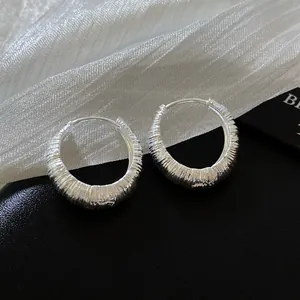 Macro view of silver-toned textured hoop earrings on elegant silk and leather.