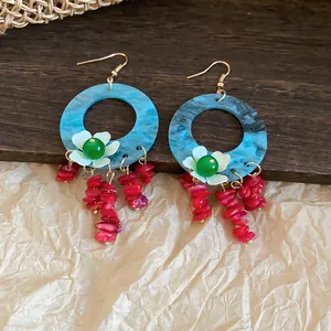 Detail view of retro flower tassel earrings with blue hoops and red stones on rustic background