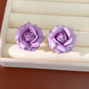 Detailed macro view of purple rose flower stud earrings on a soft velvet jewelry tray
