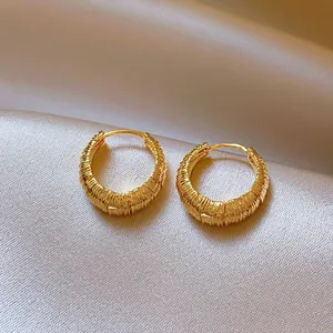 Detailed macro shot of gold round textured hoop earrings on elegant champagne silk fabric.