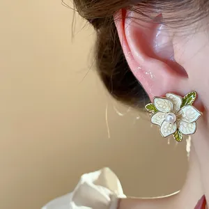 Close-up of an elegant white flower stud earring with pearl center and green leaves