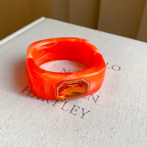 Detail of orange resin bangle featuring a large faceted gemstone and marbled texture