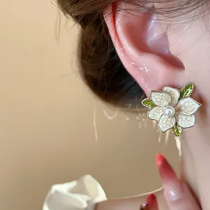 Macro view of delicate white enamel flower earring with central pearl and green leaves