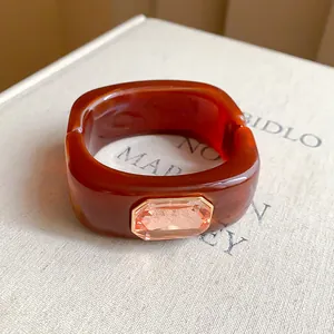 Macro view of a brown resin bangle with a large peach faceted gemstone on a textured book page