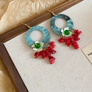 Detail of vintage earrings with blue resin hoops and red stone flower tassels.