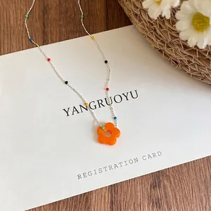 Close-up of a colorful beaded necklace with a vibrant orange flower pendant.