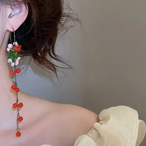Detailed view of long tassel earrings with red berries and green leaf accents