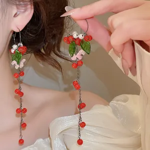 Close-up view of vintage tassel earrings with red cherry beads and green leaf details