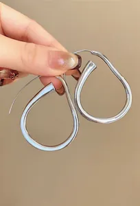Dettaglio di orecchini a cerchio irregolari a goccia color argento lucido e chic