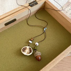 Close-up of Zen style necklace featuring a realistic acorn and dried citrus slice pendant.