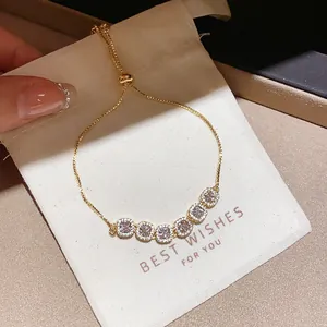 Macro view of a sparkling gold bracelet with square zircon stones on a white gift pouch.