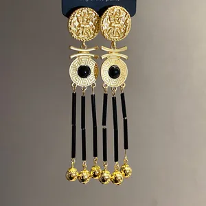 Macro view of vintage gold-tone earrings with black tassels and Greek key pattern.