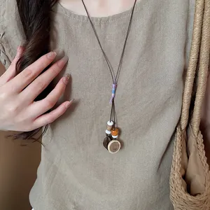 Close-up of bohemian acorn and wood disc pendant necklace worn over a beige linen shirt