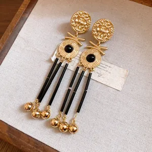 Close-up of vintage gold tassel earrings with Greek key patterns and black beads on fabric.