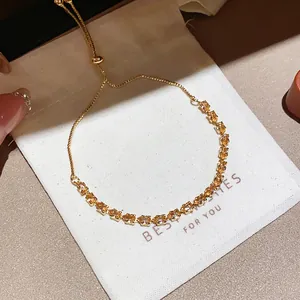 Close-up detail of a shiny gold-plated zircon flower bracelet on a white gift bag
