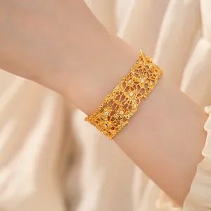 Detailed view of an ornate gold openwork lace cuff bracelet with sparkling zircon stones