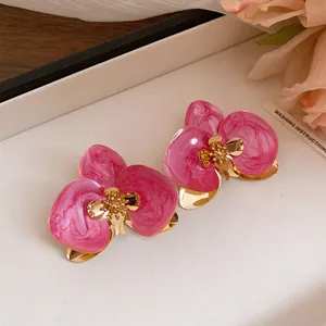 Primo piano di orecchini a perno a forma di orchidea rosa con accenti dorati e perno in acciaio.
