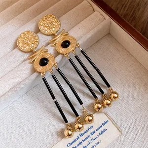 Detail view of vintage gold coin tassel earrings with black accents in a luxury jewelry box