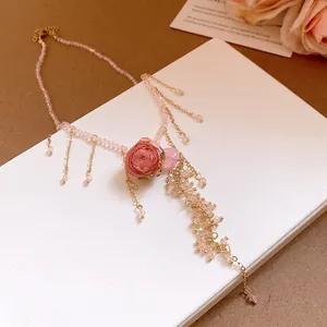 Detail view of a dainty pink rose flower necklace with beaded chain and golden tassels.