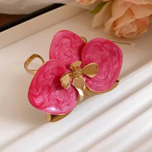 Dettaglio di orecchini a lobo a fiore in smalto rosa con eleganti dettagli in metallo dorato.