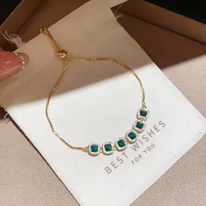 Detailed view of an elegant gold bracelet with green square zircons on a gift pouch