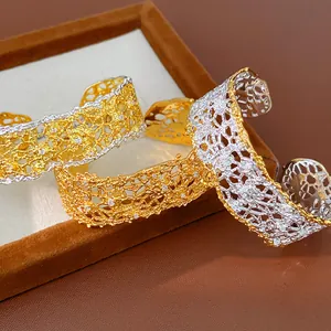 Detail view of the intricate lace hollow pattern and sparkling stones on a two-tone cuff bracelet.