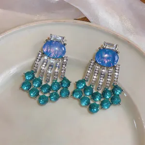 Close-up of vintage palace style earrings with blue resin and green bead tassels.