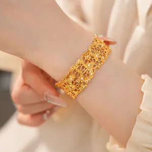 Close-up of a vintage lace-edged hollow gold cuff bracelet on a female wrist.