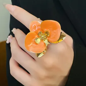 Primo piano di un grande anello a fiore in smalto arancione con dettagli oro.