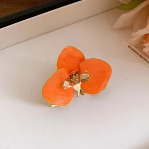 Primo piano di un raffinato orecchino a lobo vintage a fiore in smalto arancione e oro.