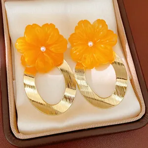 Detail of vibrant orange resin flower earrings with textured gold oval hoops in a box.