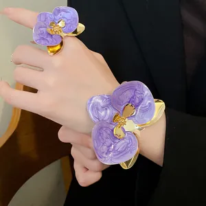 Dettaglio di elegante anello e bracciale a fiore viola marmorizzato indossati dal modello.