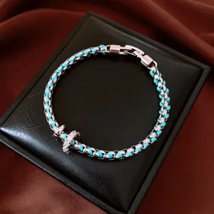 Macro detail of the turquoise braided rope and silver chain bracelet on a black box
