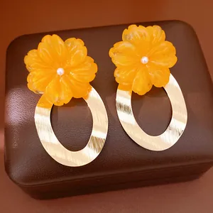 Close-up detail of oversized orange resin flower earrings with textured gold oval hoops