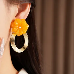 Macro detail of resin flower and gold hoop drop earrings worn on an Asian model's ear