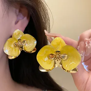 Dettaglio di orecchini a fiore di orchidea gialla con finitura in smalto e metallo dorato