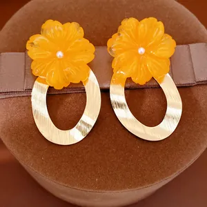 Macro view of orange resin flower earrings with elegant brushed gold oval hoop design